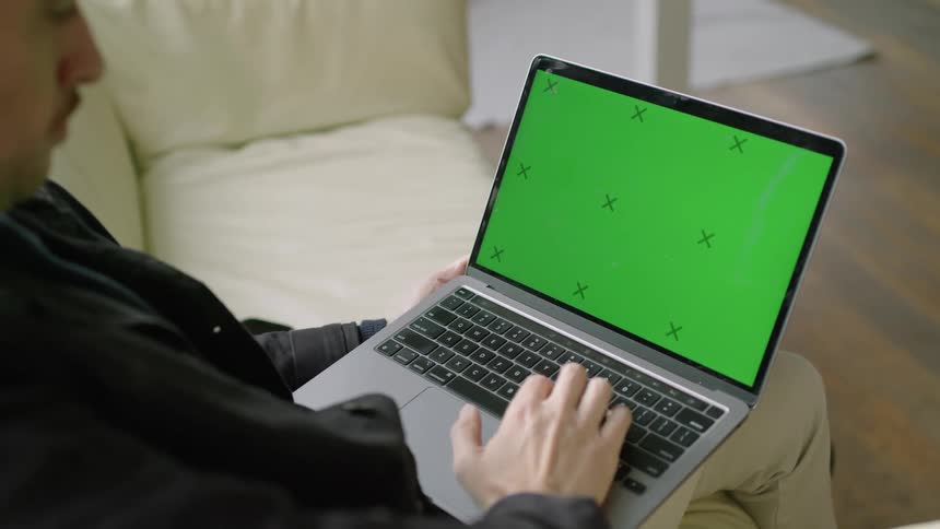 A man typing on a laptop while sitting on a living room sofa