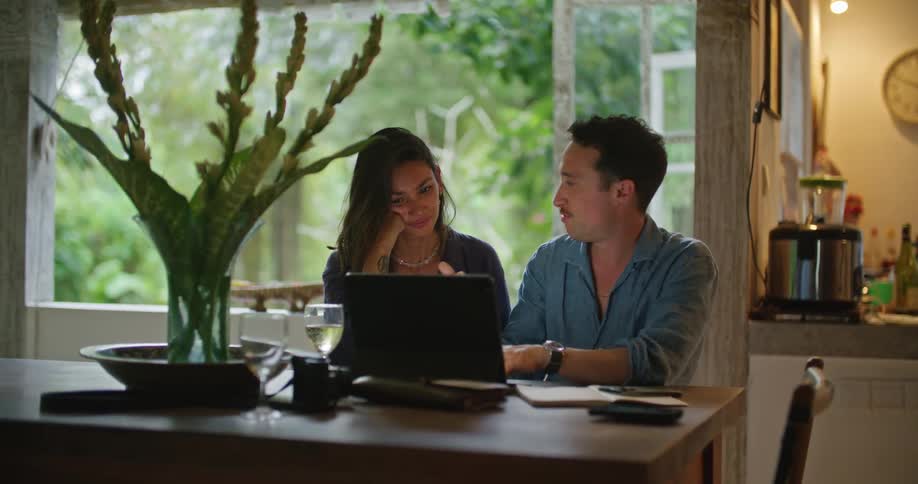 A man and a woman are sitting together at a table with a laptop computer talking and looking at the screen