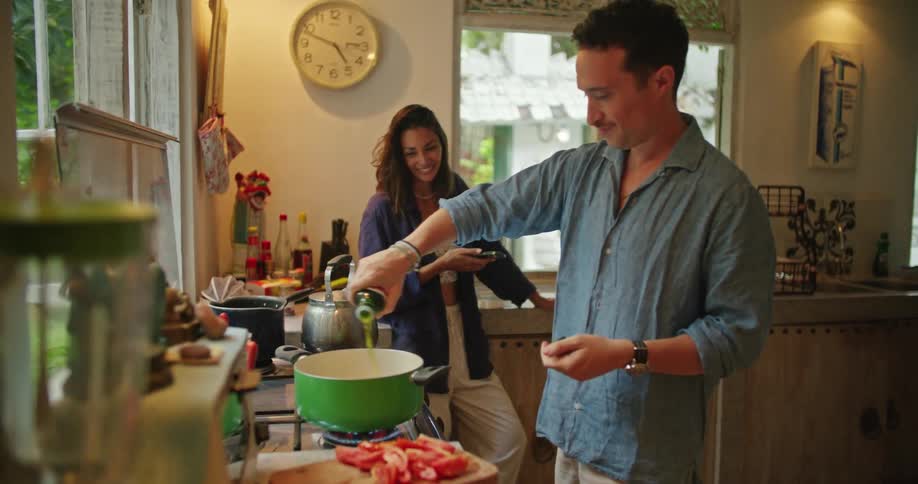 Woman uses her smartphone and talks with man cooking at nearby stove