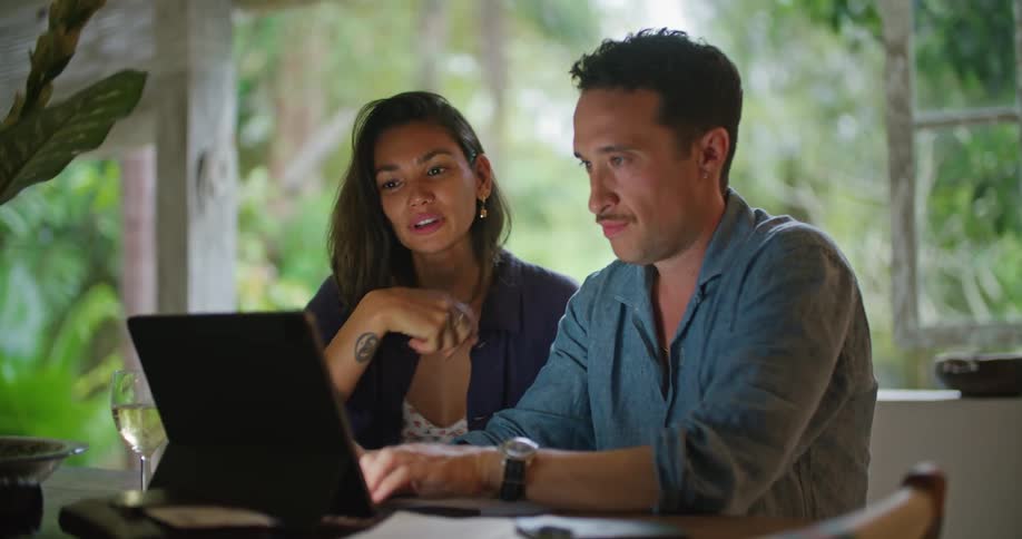 A man and a woman are sitting together at a table with a laptop computer talking and looking at the screen