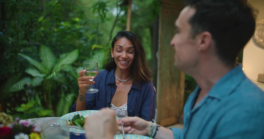 Happy couple eating a meal and drinking white wine on a dinner table in the patio