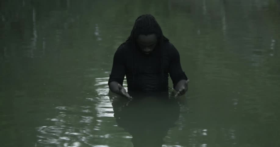 A man stands fully clothed in a lake