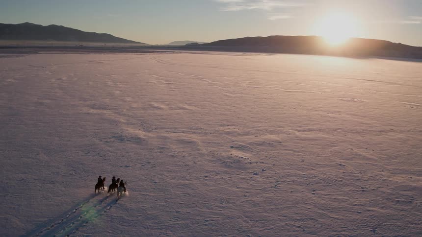 Three people ride horses at dawn