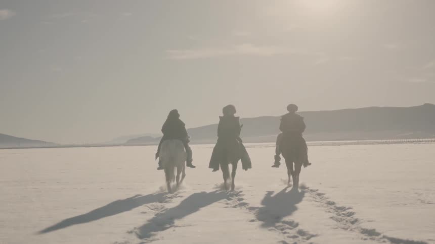 Three people on horses walk in the snow