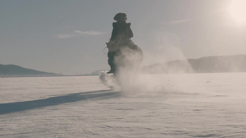 A man in heavy clothing rides a horse through the snow