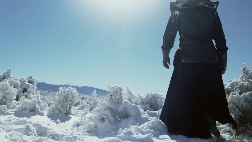 A man dressed as a warrior walks through a snowy area in the mountains