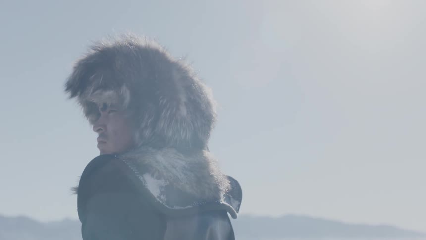 A man wearing a fur hat stands outside in the sun