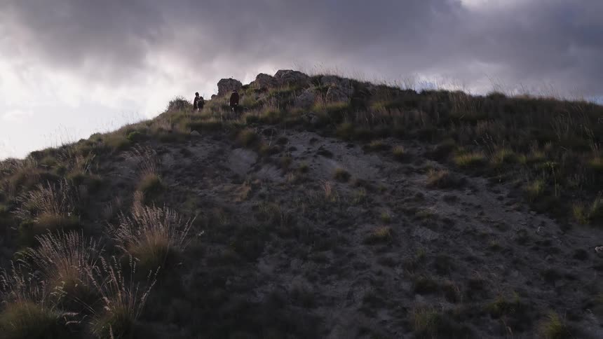 Three people standing on a hillside under grey clouds