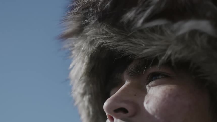 A man wearing a fuzzy hat standing outside on a sunny day