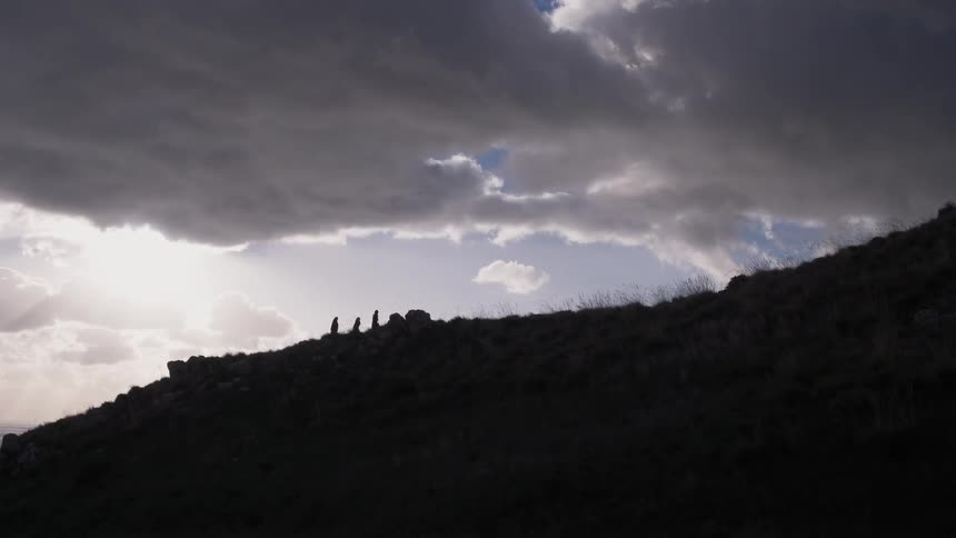 Three men in heavy clothing walk on a hillside on a cloudy evening