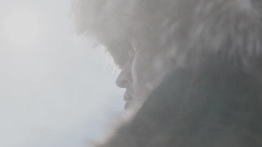 A man wearing fur stands outside on a cloudy day