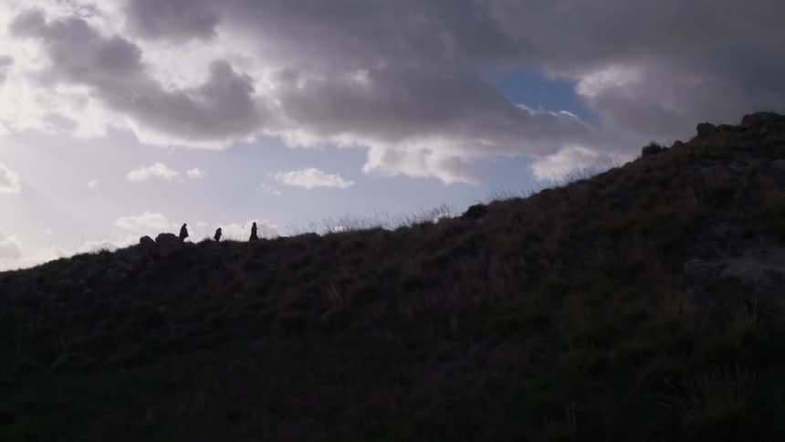 Three men in heavy clothing walk on a hillside on a cloudy evening