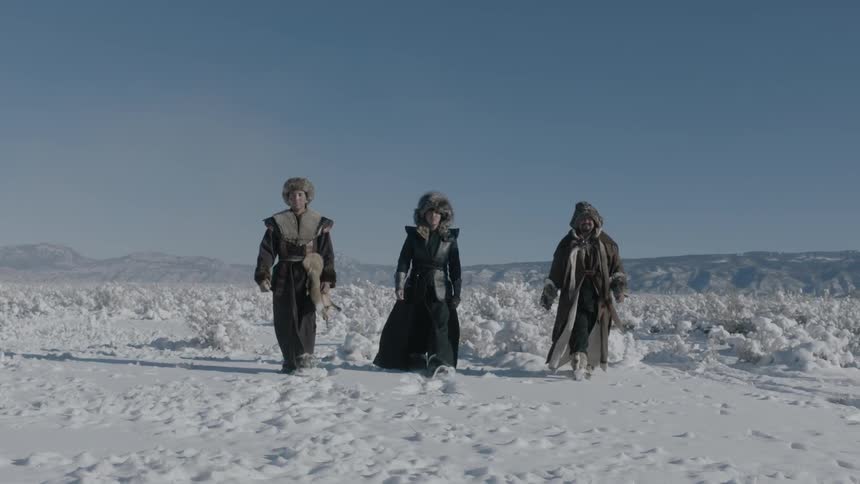 Three people are walking over a snow covered field