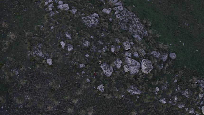 People climbing down a large hill with rocks and trees