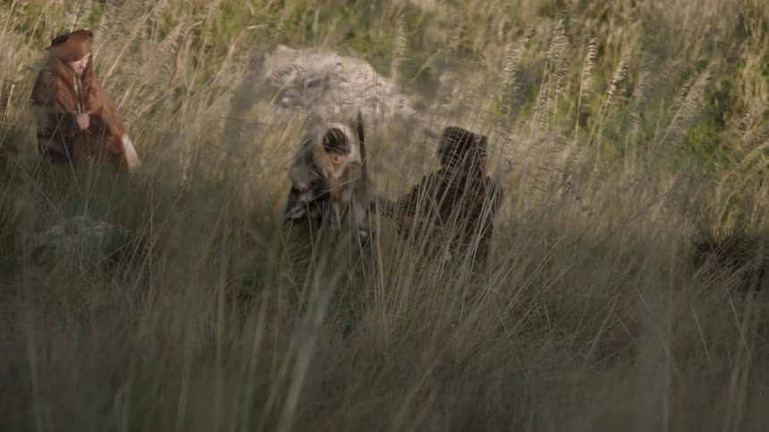 People are hiking through tall grass on a windy day