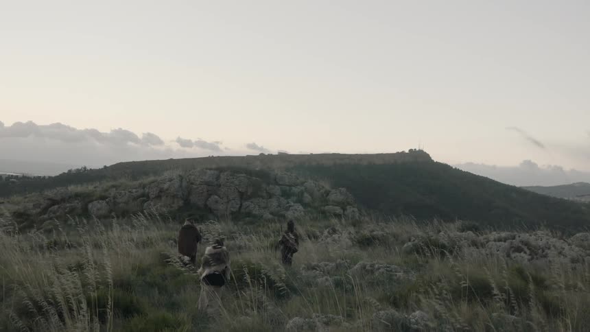 Three people stand outside on a scrubby hill