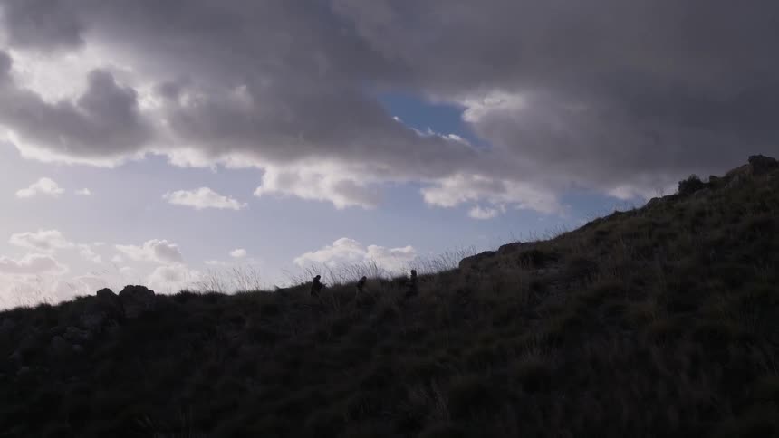 People hike up a dark hill on a cloudy day