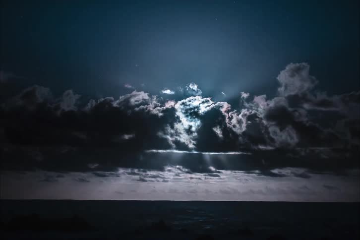 The moon behind storm clouds over the ocean