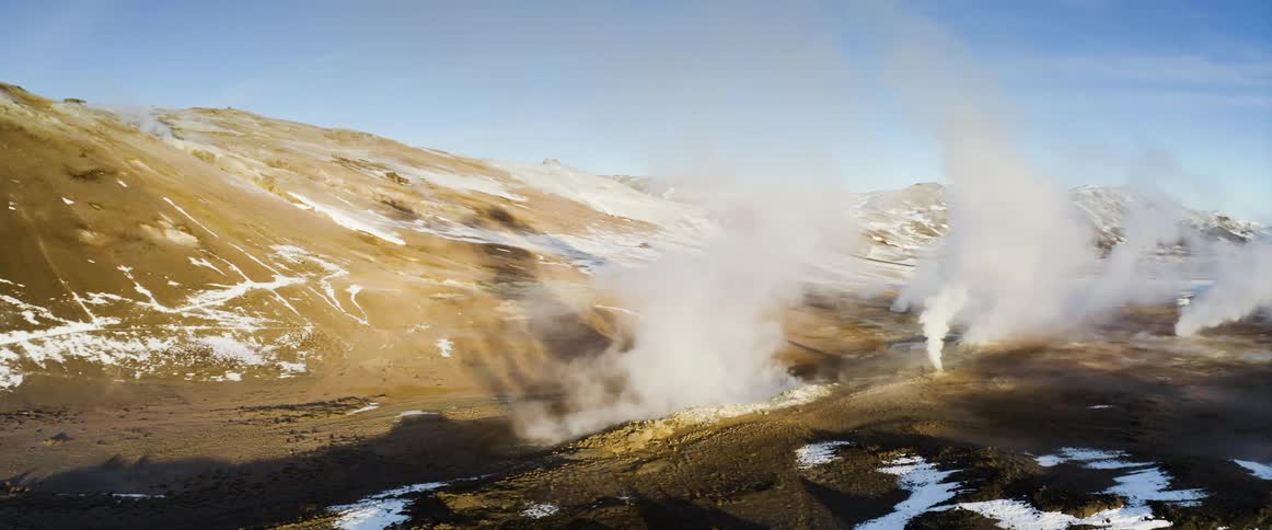 Smoke rises from geysers at the bottom of a canyon