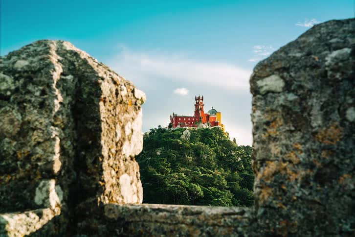 A red castle is on top of a mountain as clouds float in the sky