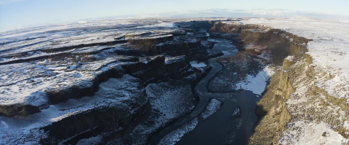 An aerial view of a river flowing through a snowy canyon in winter