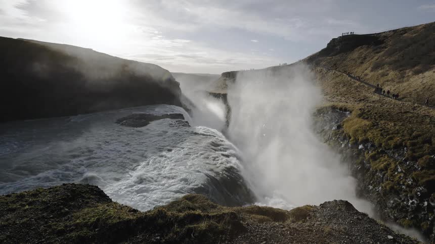 A river flows into a canyon sending a cloud of mist into the air in the countryside during the day