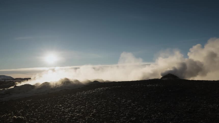 White clouds of steam rising from the ground on the frozen plains at evening under a blue sky