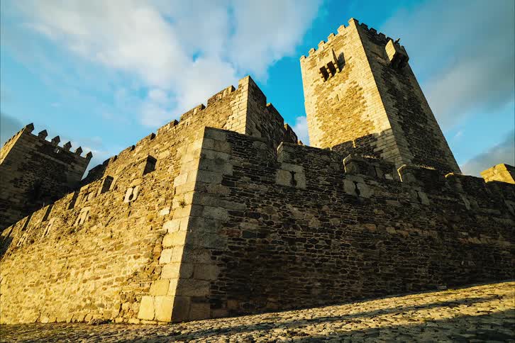 Vehicle speeds past crenelated fortification under a cloudy sky