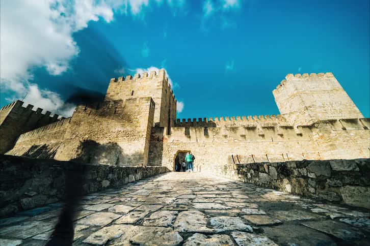 Tourists walk across a bridge into a castle
