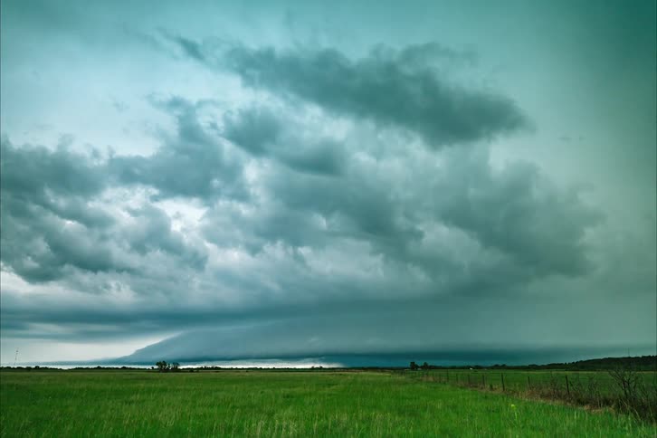 A storm moves over a rural field as lightning flashes in the sky and storm clouds are in rotation on the ground