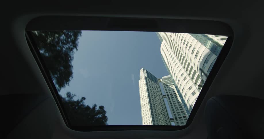 Skyscrapers on the city skyline seen from the open sun roof of a car driving in the city