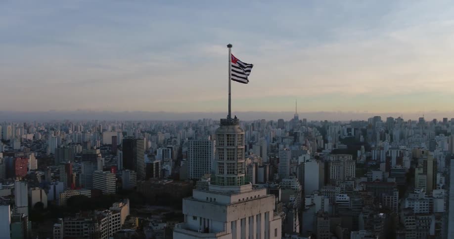 Camera pans around a flying flag on a flagpole high atop a building