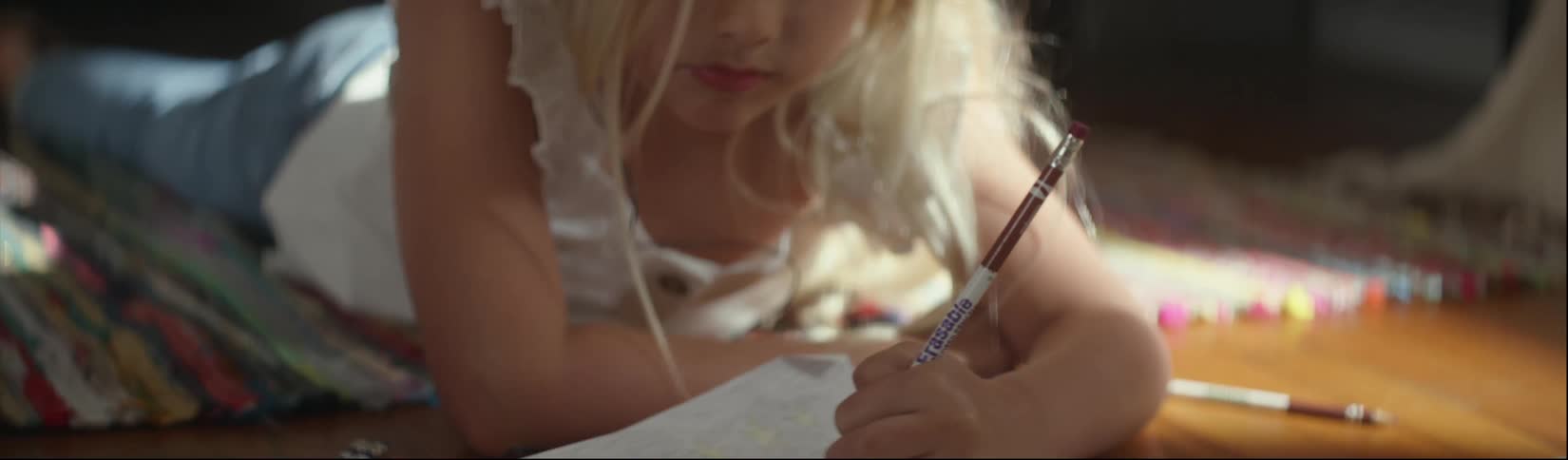 A little girl using colored pencils to draw while lying on the floor