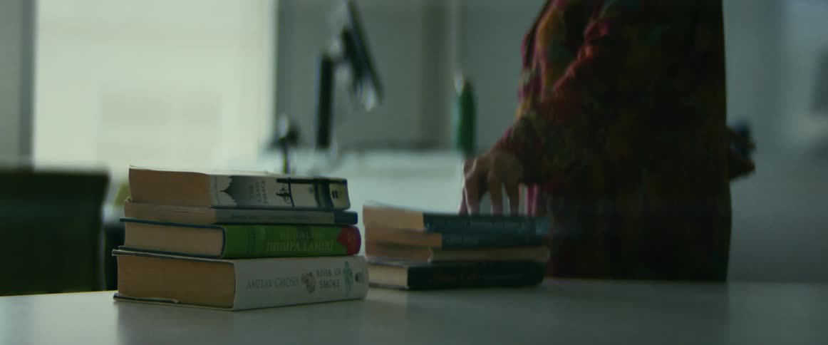 University teacher puts a pile of books over a desk and walks towards the students