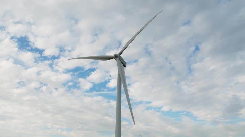 Blades on wind turbines rotate slowly under a heavily clouded sky