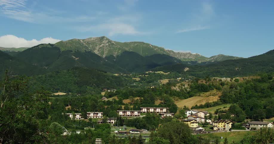 Buildings of a small town on the gentle hill slopes next to a mountain covered in green lush vegetation