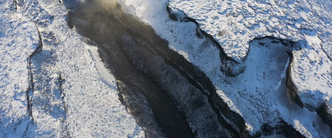 A layer of snow covers the ground surrounding an iced over river