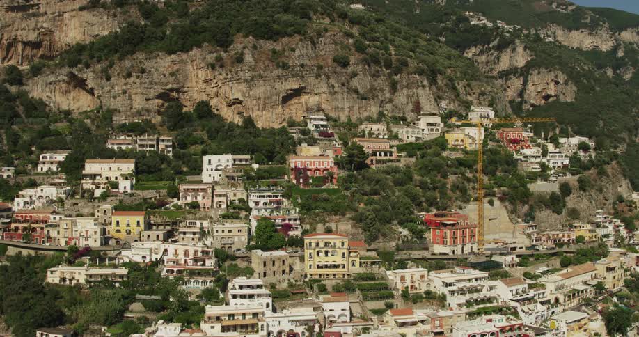 A small town with somewhat dilapidated houses and buildings has cars shown very far away driving on a road going across the town