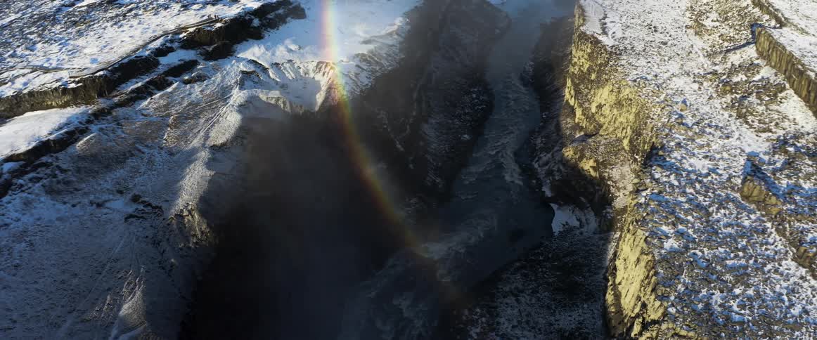 A rainbow over a canyon with a flowing river and melting snow on a bright sunny day