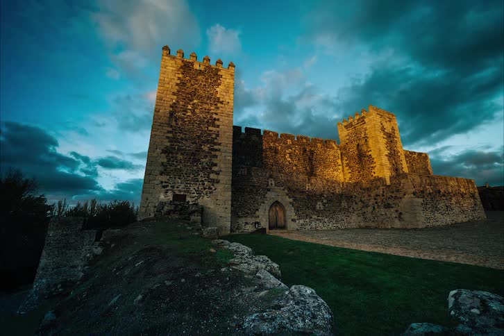 The sun shining on a stone castle on a hill with sky and day darkening