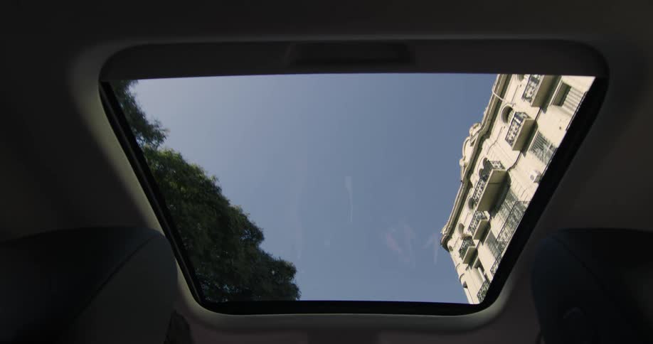 City buildings seen through the sunroof of a car driving at daytime
