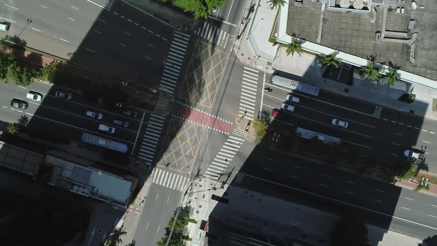 An aerial view of a person crossing the street and another riding a bike in a city with vehicles driving on the streets