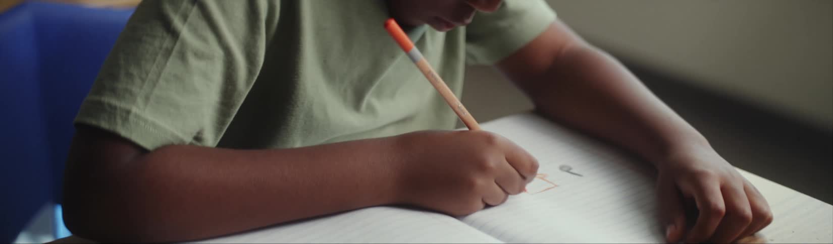 Child focused on his homework makes a drawing using colored pencils