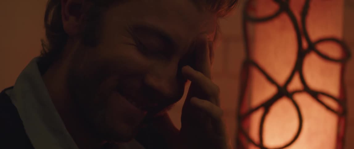 Close up of the face of a young bearded man laughing while listening to someone out of frame