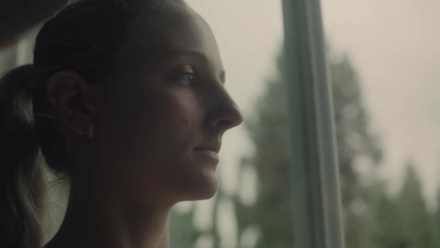 A woman is standing inside next to a window