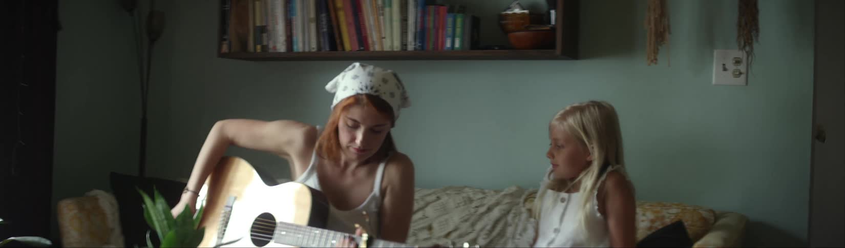 Little girl brings an acoustic guitar to her mother sitting in the couch at home