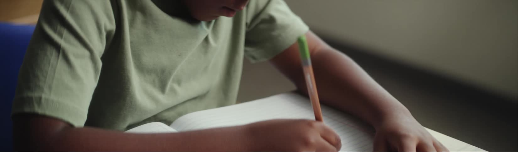 Male student with green t shirt sits at desk writing in notebook