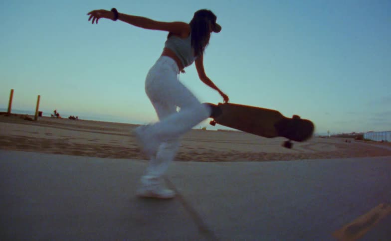 Young woman rides a skateboard on a road in the beach next to the ocean caught on vintage film