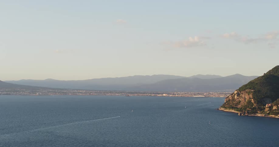 A boat leaves a wake in the calm ocean near the hilly coast line