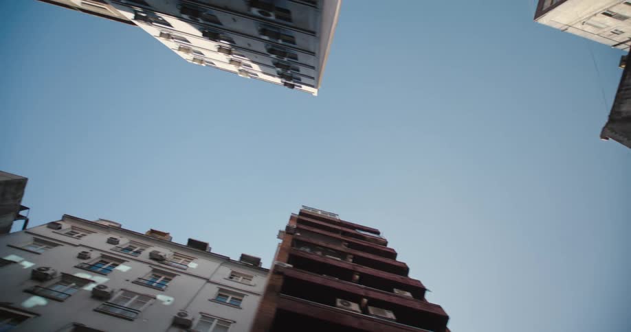 Camera pointing straight up tracks down a street or alley past tall buildings